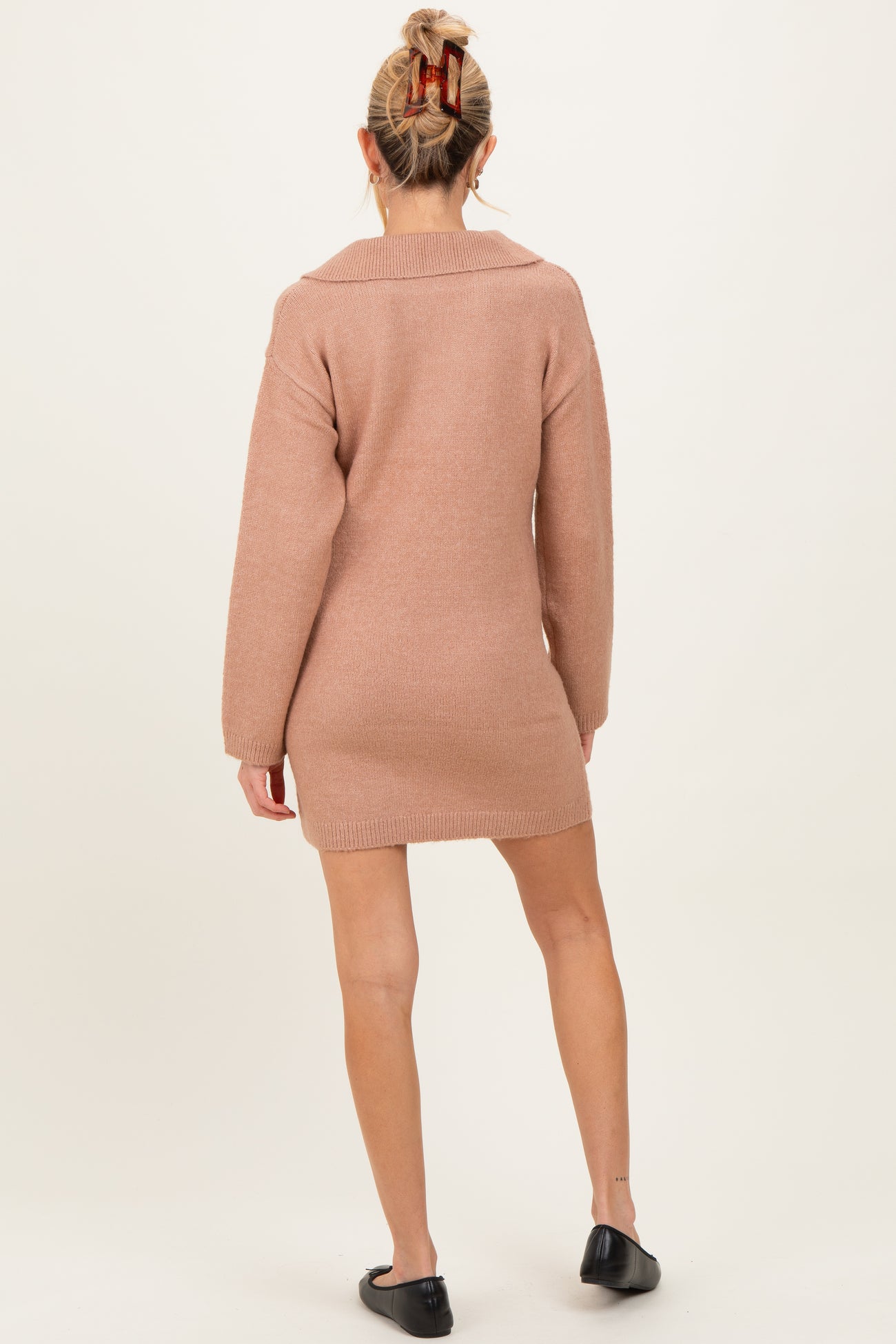 woman wearing a blush pink maternity sweater dress with a collar, showing her back and legs, styled with black flats