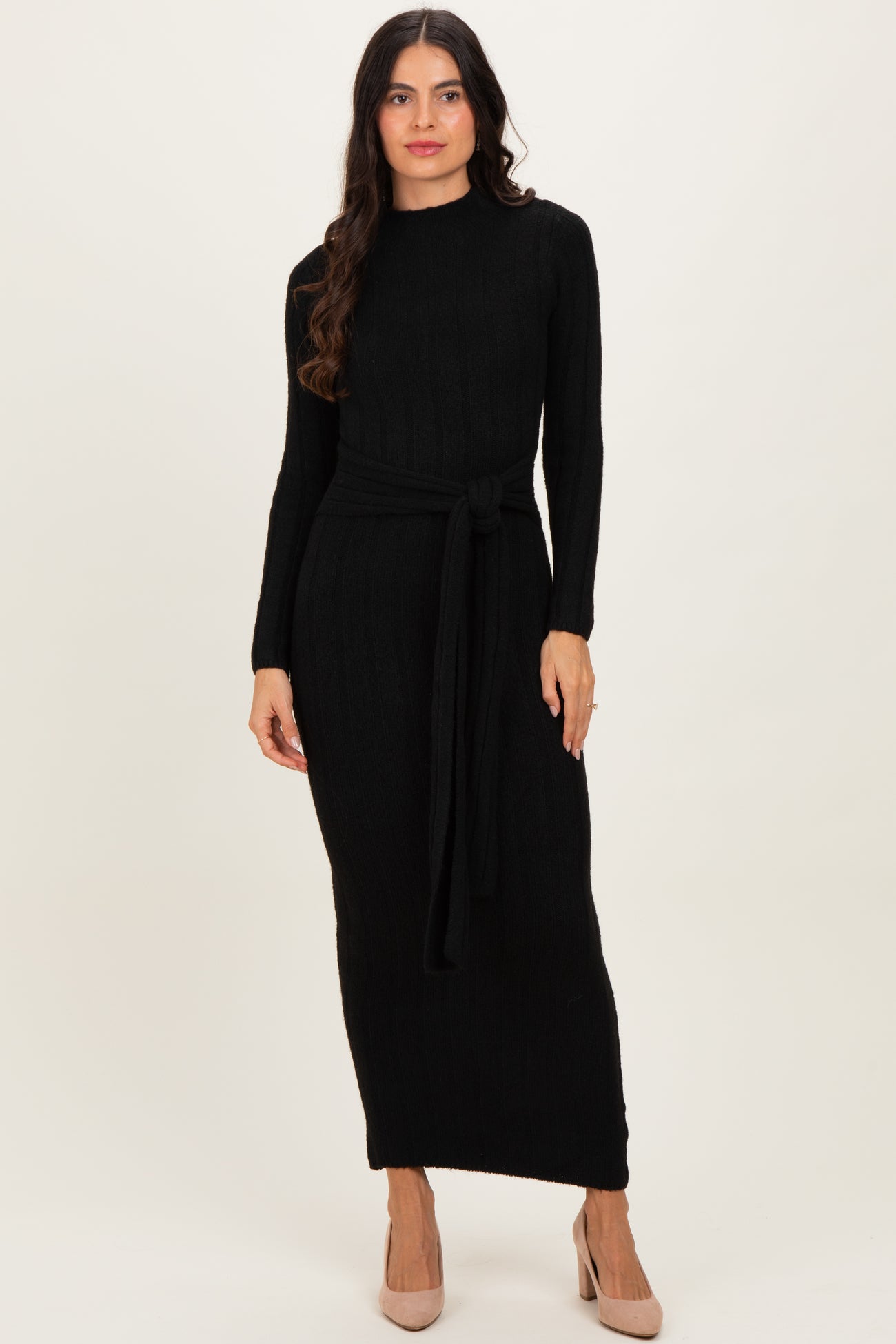 woman wearing a black long sleeve ribbed knit maxi dress with a tie waist detail and beige heels