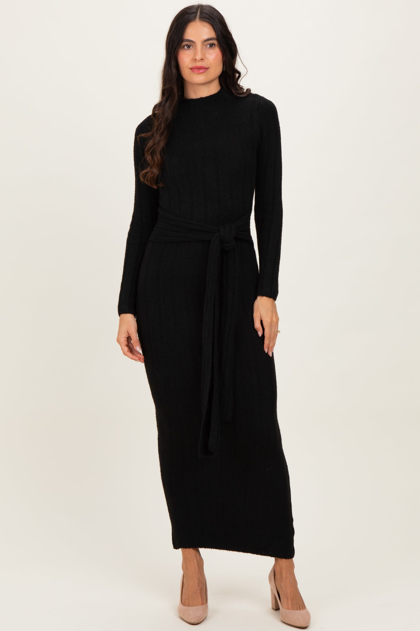 woman wearing a black long sleeve ribbed knit maxi dress with a tie waist detail and beige heels