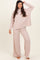 woman wearing a light pink ribbed long sleeve top and matching wide-leg pants, standing barefoot with a playful pose