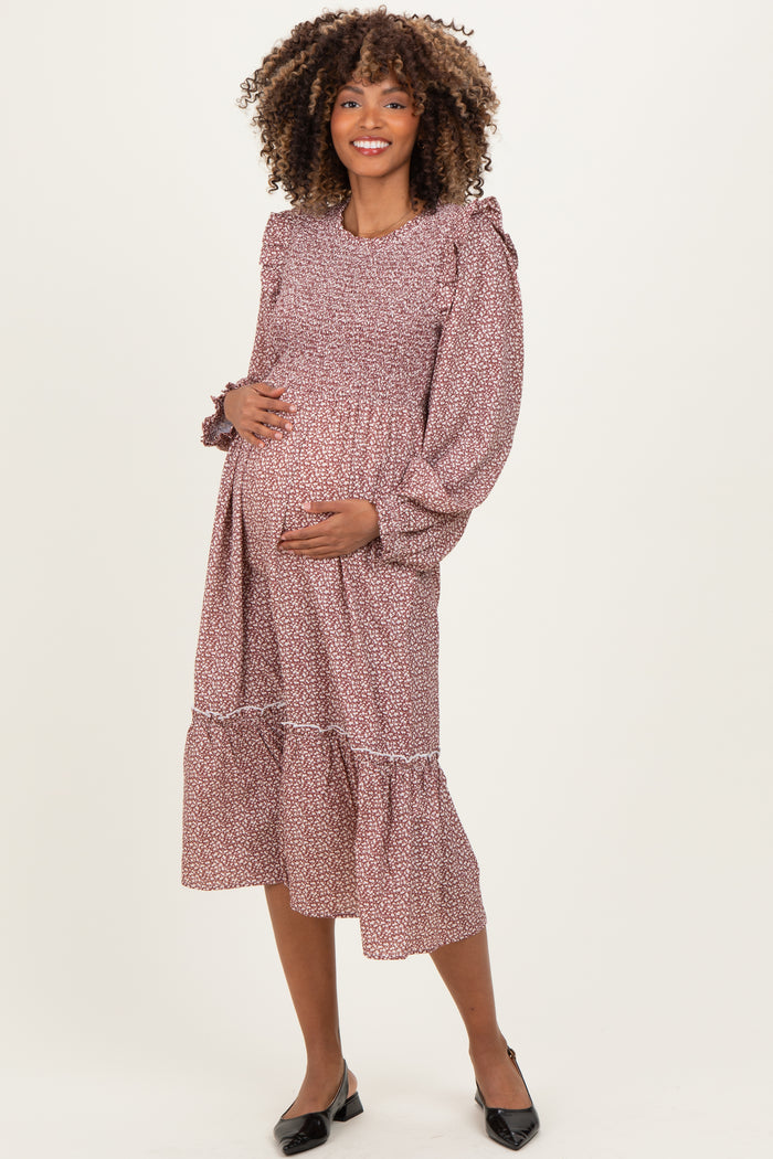 woman wearing a burgundy floral print maternity dress with long puff sleeves and a tiered hem, holding her baby bump