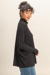 woman wearing a black long sleeve turtleneck top and blue jeans, with her hair in a messy bun and a soft smile