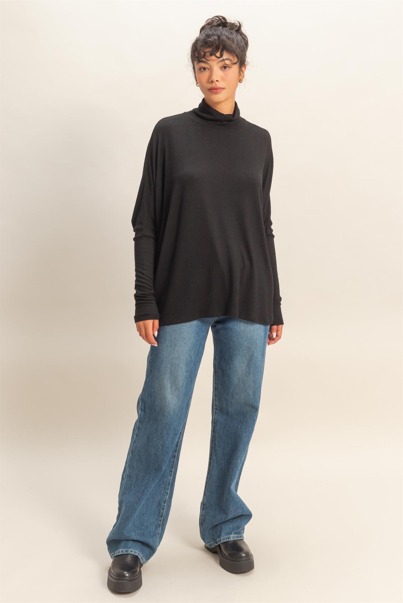 woman wearing a black long sleeve turtleneck top with relaxed fit and high-waisted blue wide-leg jeans