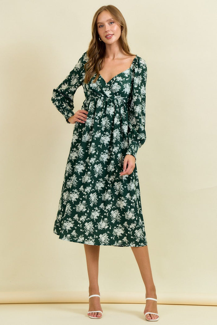 woman wearing a green floral midi dress with long sleeves and a v-neckline, standing against a light background
