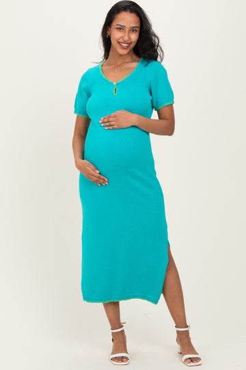 woman wearing a turquoise maternity knit dress with short sleeves and side slits, holding her baby bump