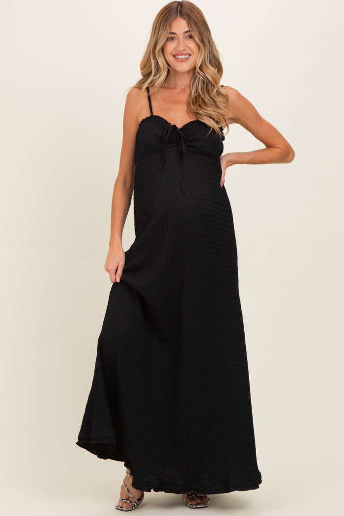 woman wearing a black maternity maxi dress with a tie detail at the bust and a side slit, showing off her baby bump