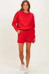 woman wearing a red sweatshirt and matching red shorts with pockets and a drawstring, styled with white sneakers