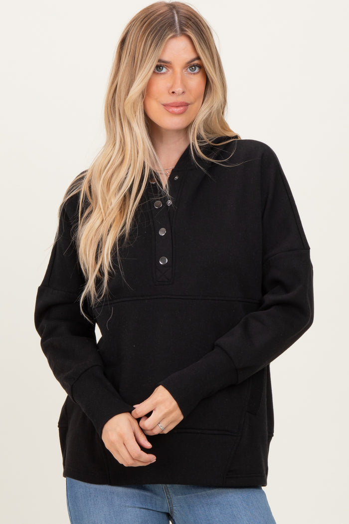 woman wearing a black long sleeve pullover sweatshirt with button details and a front pocket, styled with jeans