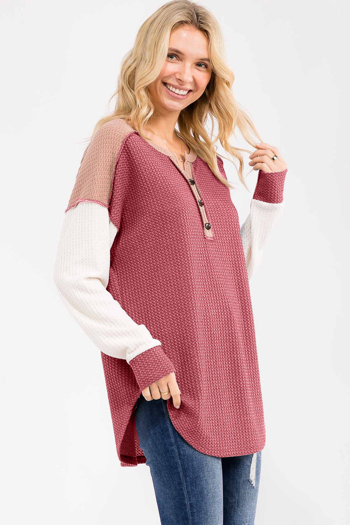 woman wearing a maroon and cream color-blocked long sleeve henley top with buttons and side slits, paired with jeans