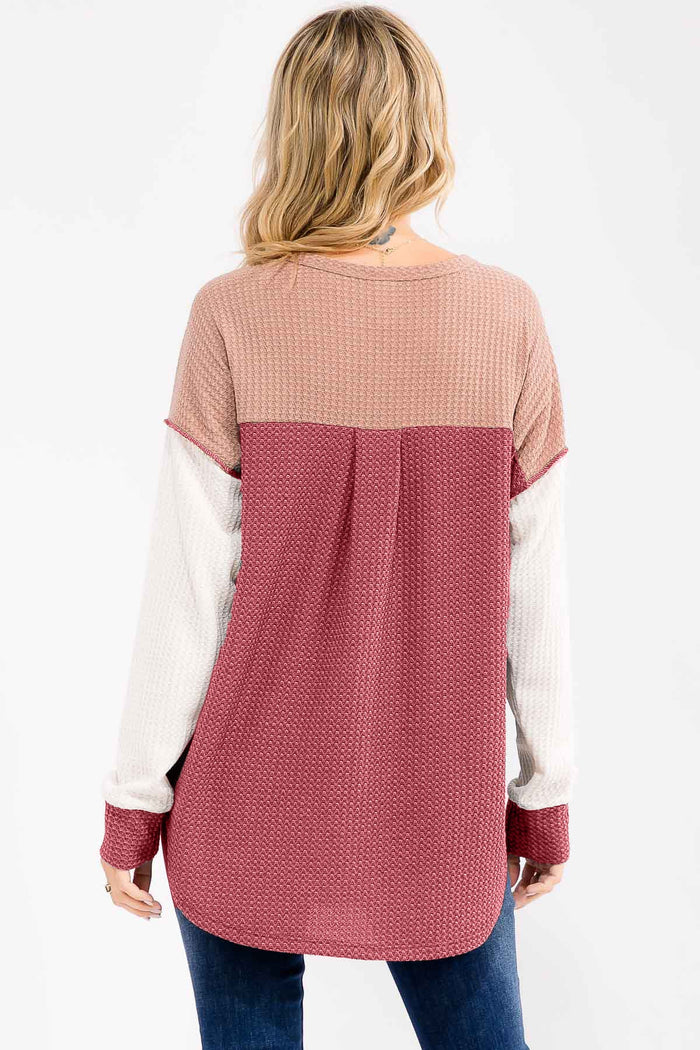 woman wearing a color-blocked long sleeve top in burgundy, beige, and cream with a curved hem and relaxed fit