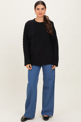 woman wearing a black cable knit sweater and wide leg jeans, standing against a neutral background