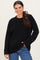 woman wearing a black cable knit sweater with long sleeves and a relaxed fit, smiling with one hand in her pocket