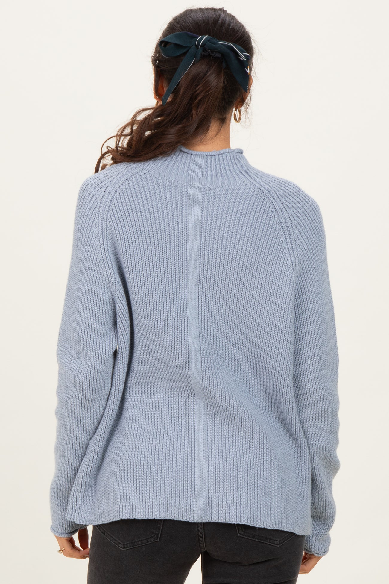 woman wearing a light blue ribbed sweater with a high neckline and long sleeves, viewed from the back