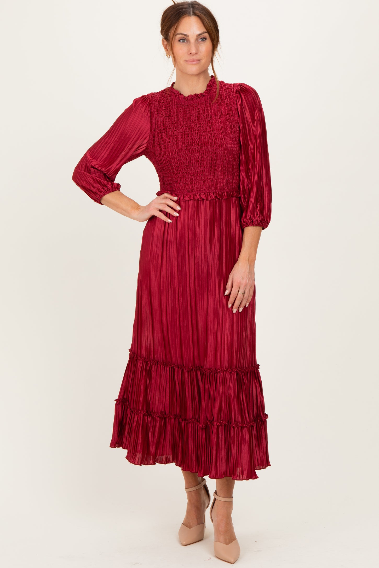 woman wearing a burgundy pleated midi dress with smocked bodice and ruffle hem, posing with one hand on her hip