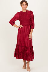 woman wearing a burgundy pleated midi dress with smocked bodice and ruffle hem, posing with one hand on her hip