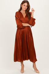 woman wearing an rust-colored pleated midi dress with long sleeves and a v-neckline, styled with beige heels