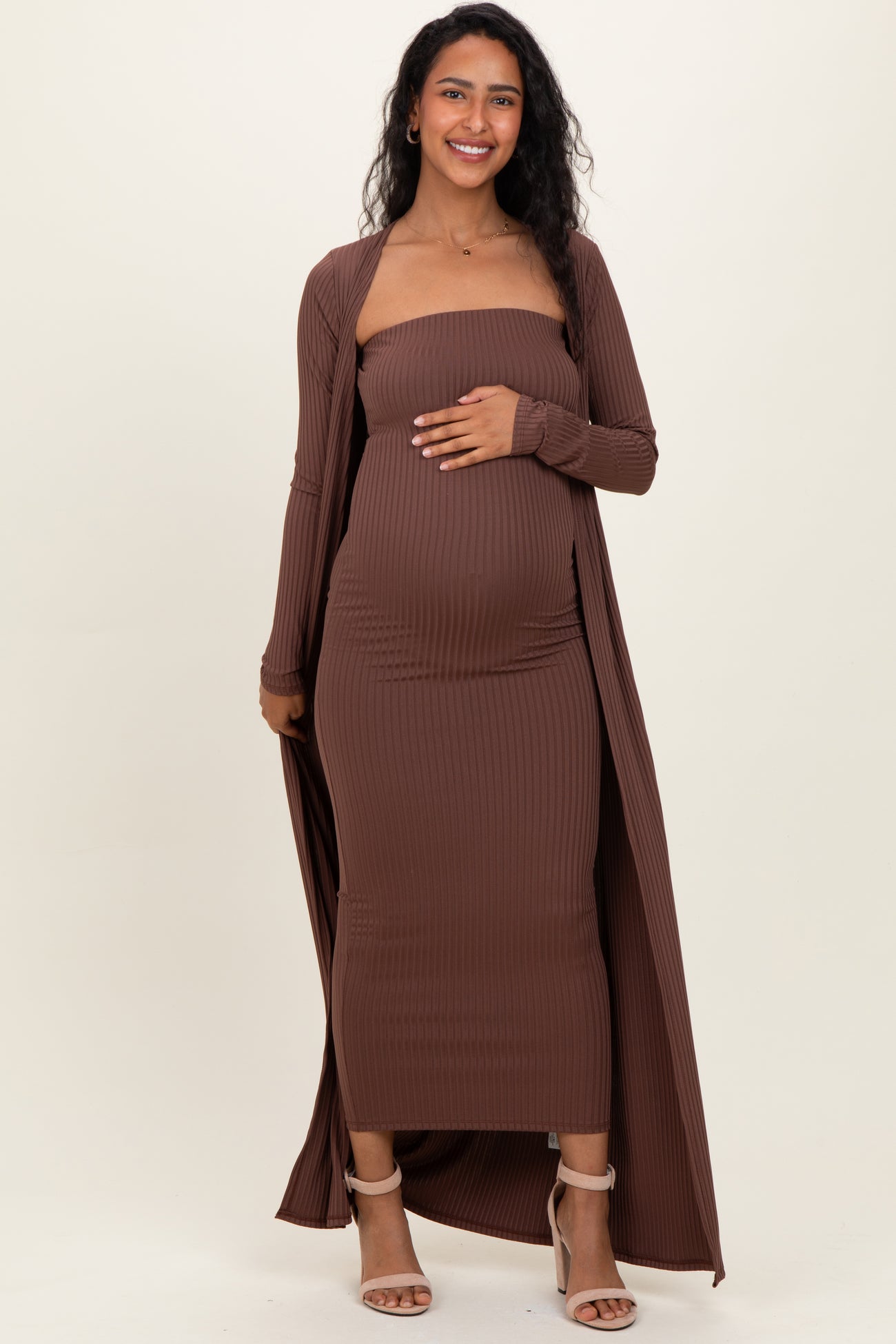 woman wearing a brown ribbed maternity dress with a long cardigan, gently holding her baby bump