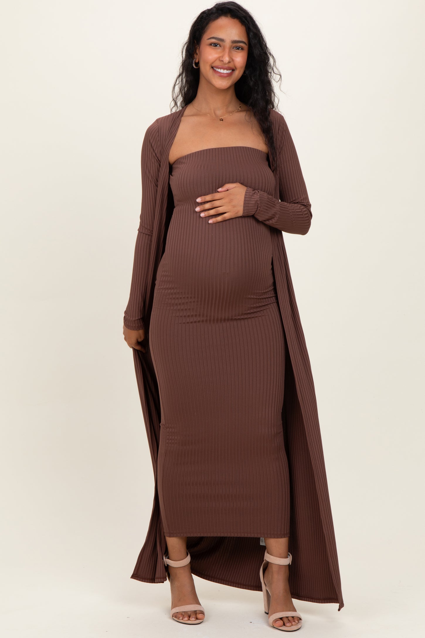 woman wearing a brown ribbed maternity dress with a long cardigan, gently holding her baby bump