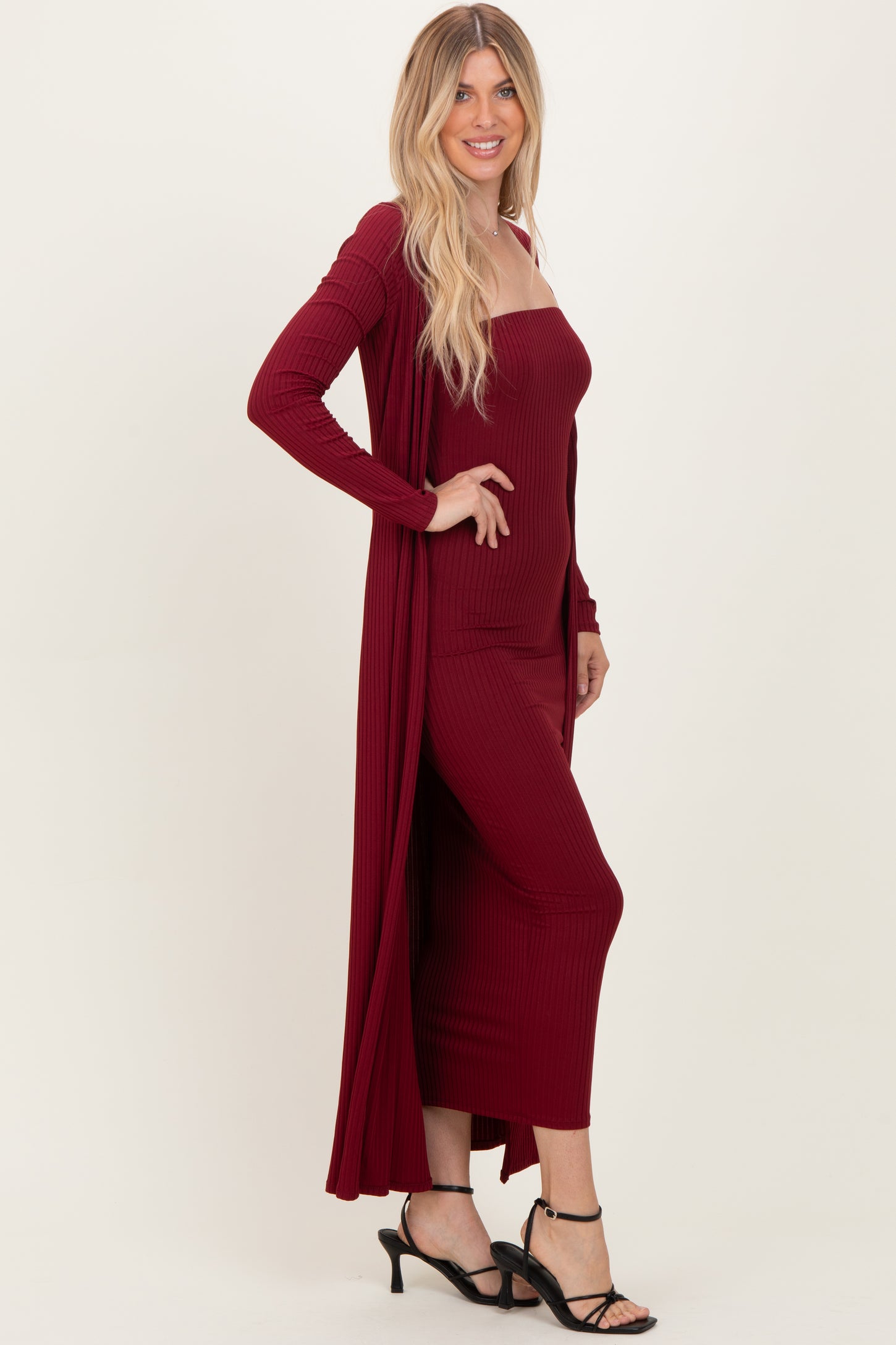 woman wearing a burgundy ribbed maxi dress with matching long cardigan and black strappy heels