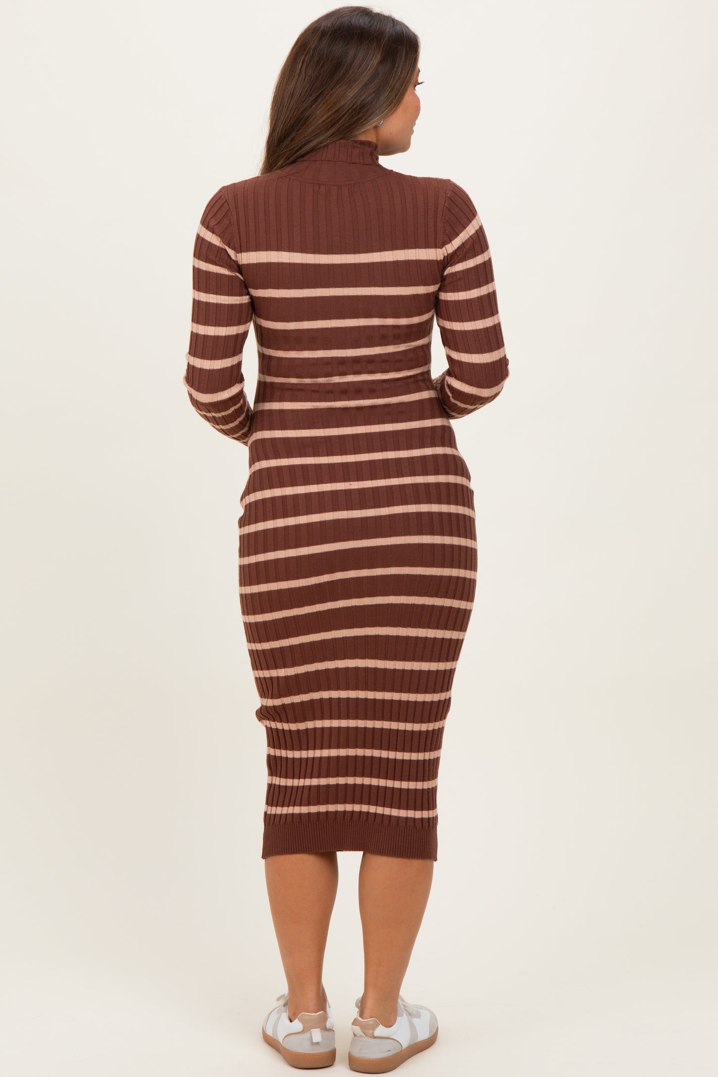 woman wearing a rust and beige striped maternity dress with a fitted silhouette and long sleeves, showing a baby bump