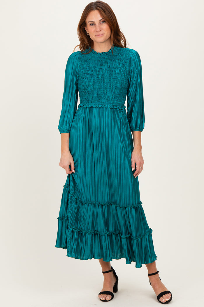 woman wearing a teal pleated midi dress with a smocked bodice and ruffle hem, paired with black strappy heels