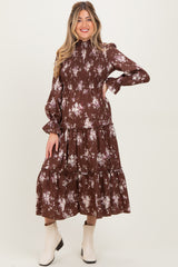 woman wearing a brown floral maternity dress with long sleeves and tiered ruffle hem, highlighting a baby bump