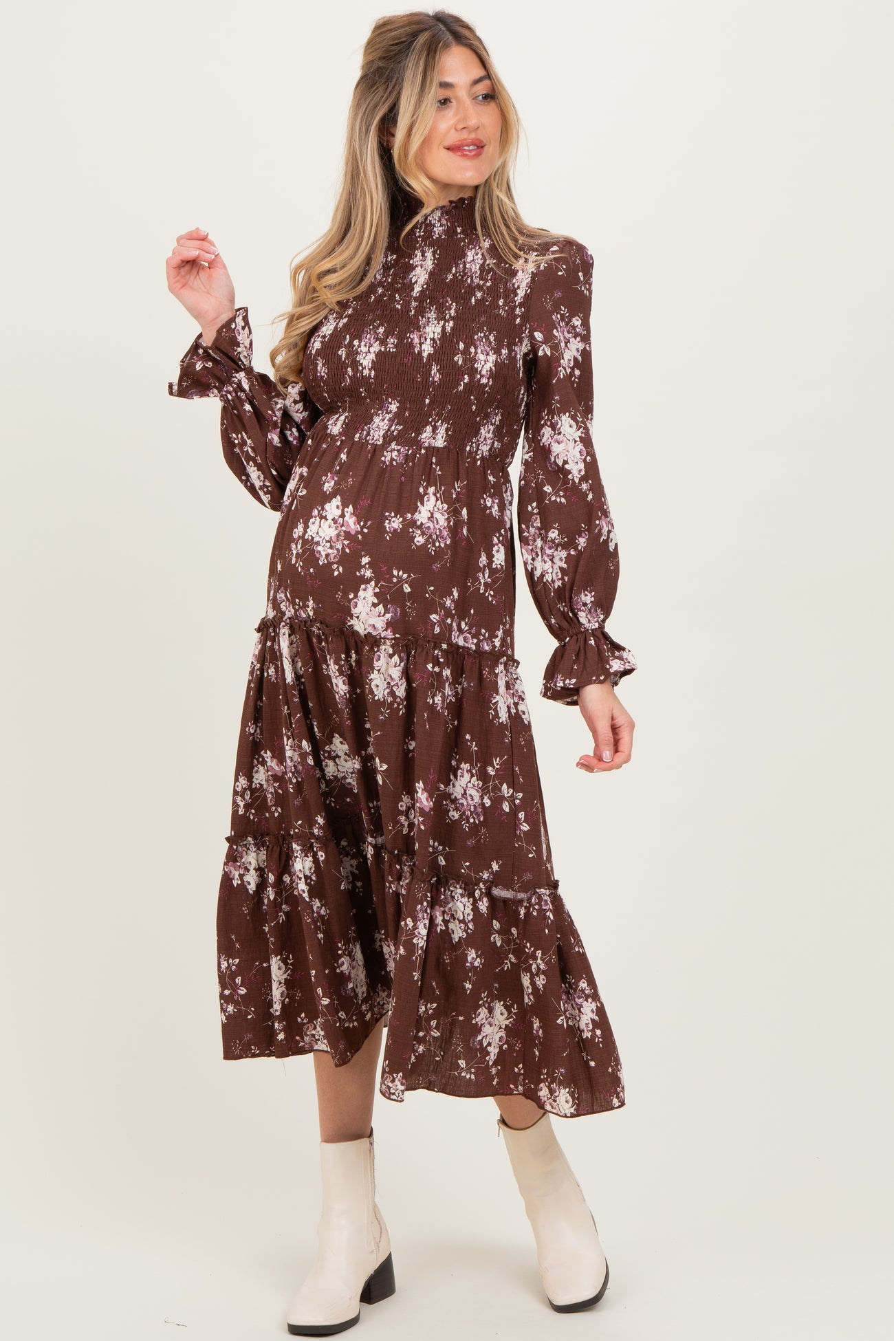 woman wearing a brown floral print maternity dress with long sleeves and a tiered skirt, showing her baby bump