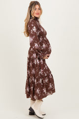 woman wearing a brown floral maternity dress with long sleeves and a flowing skirt, showing her baby bump