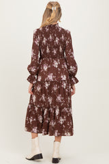 woman wearing a brown floral maternity dress with tiered design and long sleeves, viewed from the back