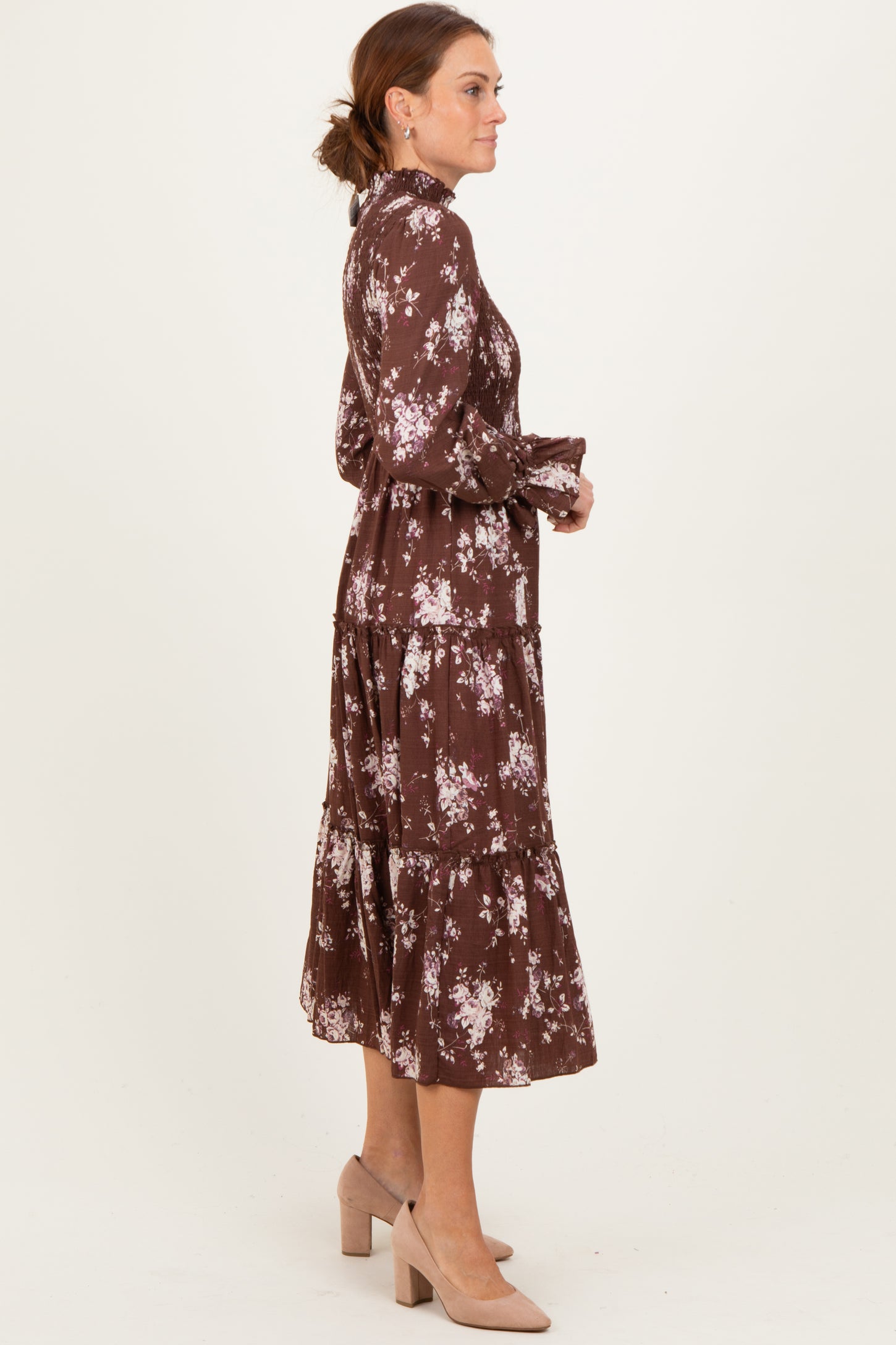 woman wearing a brown floral tiered midi dress with long sleeves and a side profile view