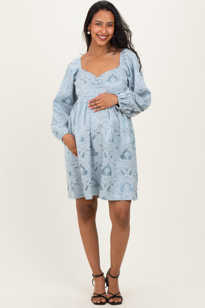 woman wearing a light blue patterned maternity dress with a square neckline and long sleeves, holding her baby bump