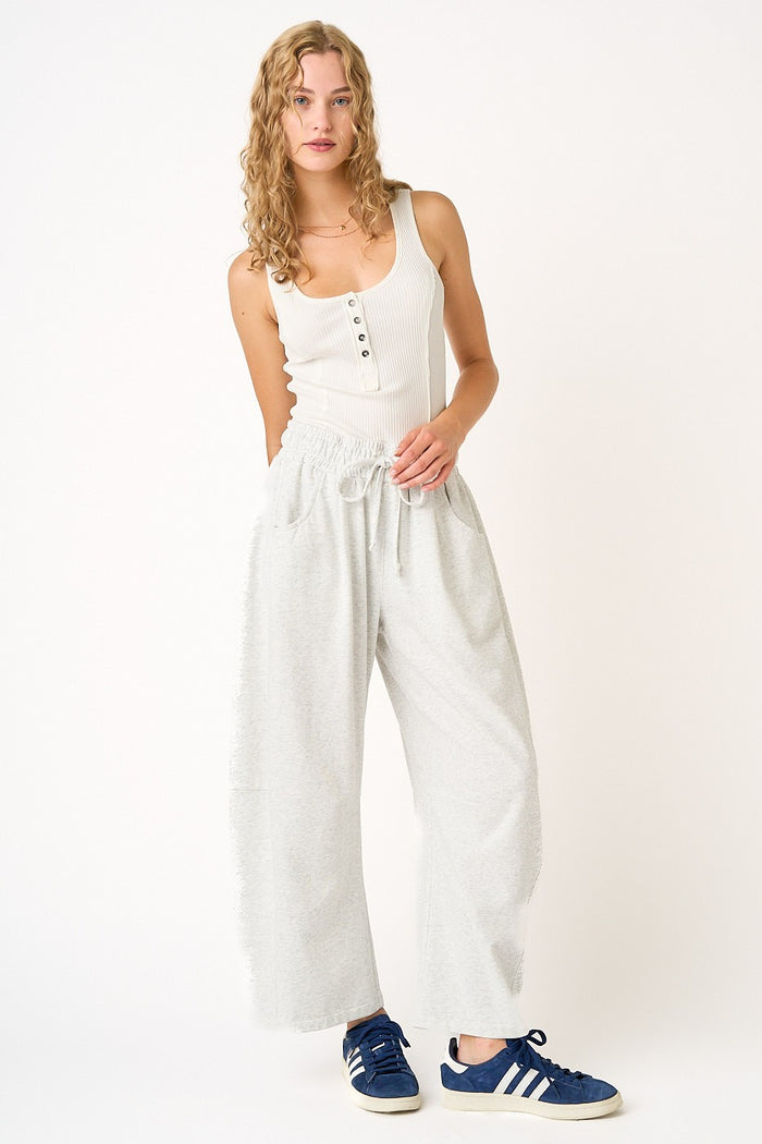 woman wearing a white ribbed tank top and light gray wide-leg sweatpants with an elastic waistband and drawstring.