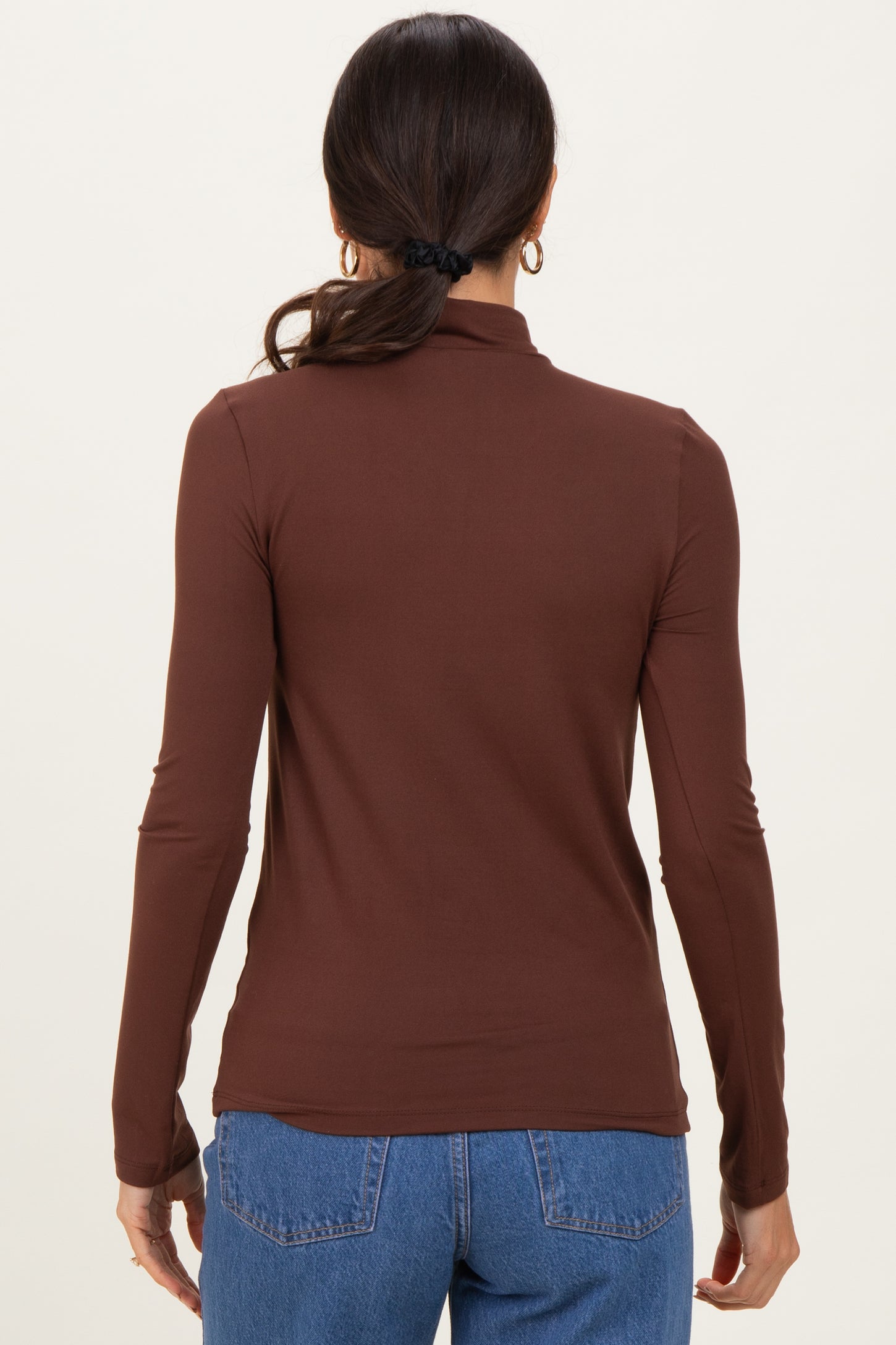 woman wearing a fitted brown long sleeve top with a mock neck and styled hair in a ponytail, viewed from the back