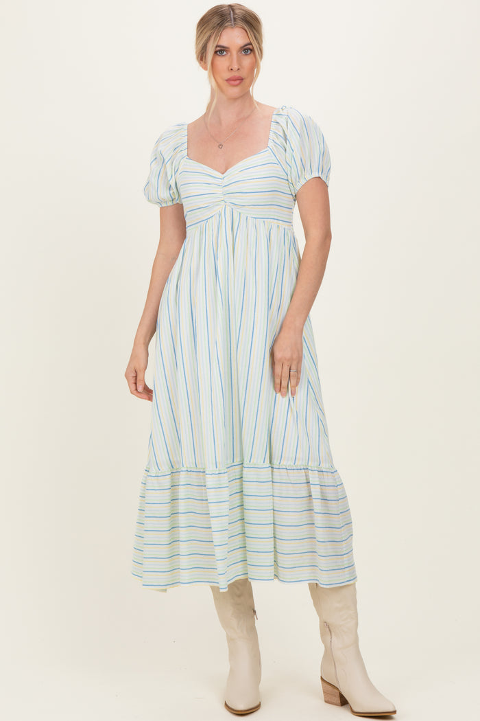 woman wearing a light blue and white striped puff sleeve maxi dress with a tiered skirt and beige knee-high boots
