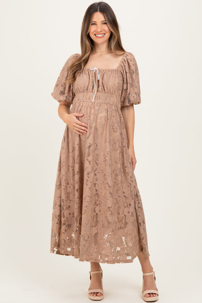 woman wearing a blush lace maternity dress with puff sleeves and a tie detail, holding her baby bump