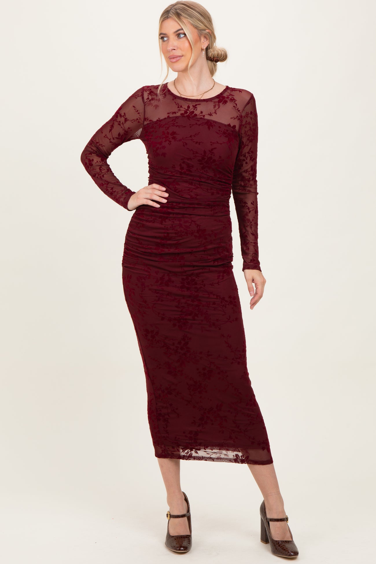 woman wearing a burgundy long sleeve bodycon dress with floral lace details and a fitted silhouette
