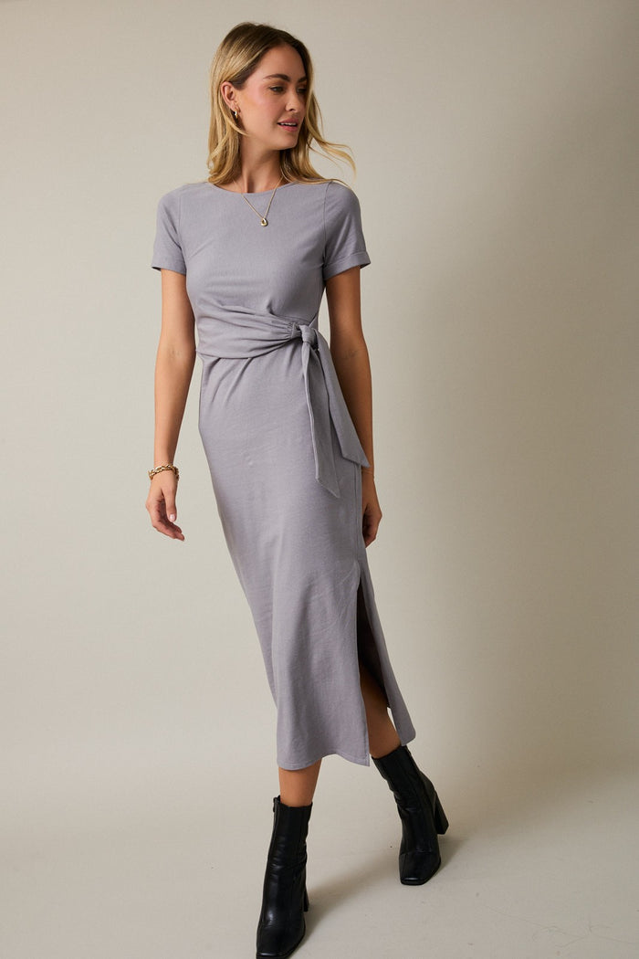 woman wearing a gray midi dress with short sleeves and a side tie detail, paired with black ankle boots