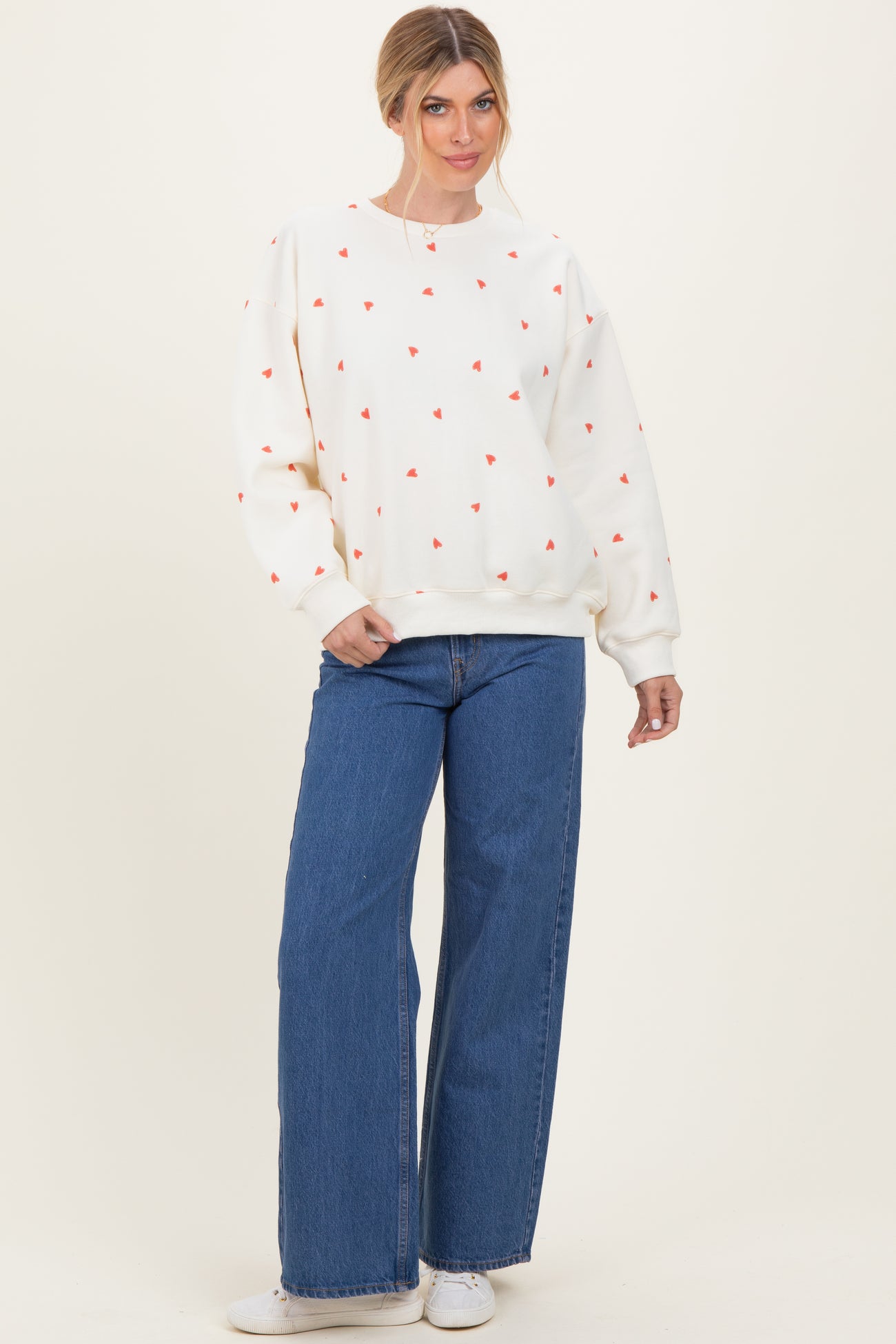 woman wearing a cream sweatshirt with red heart patterns and blue wide-leg jeans
