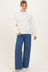 woman wearing a cream sweatshirt with red heart patterns and blue wide-leg jeans