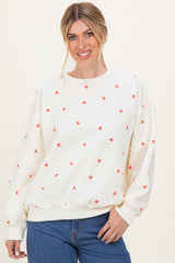 woman wearing a cream sweatshirt with red heart print and relaxed fit, smiling while posing with hands in front