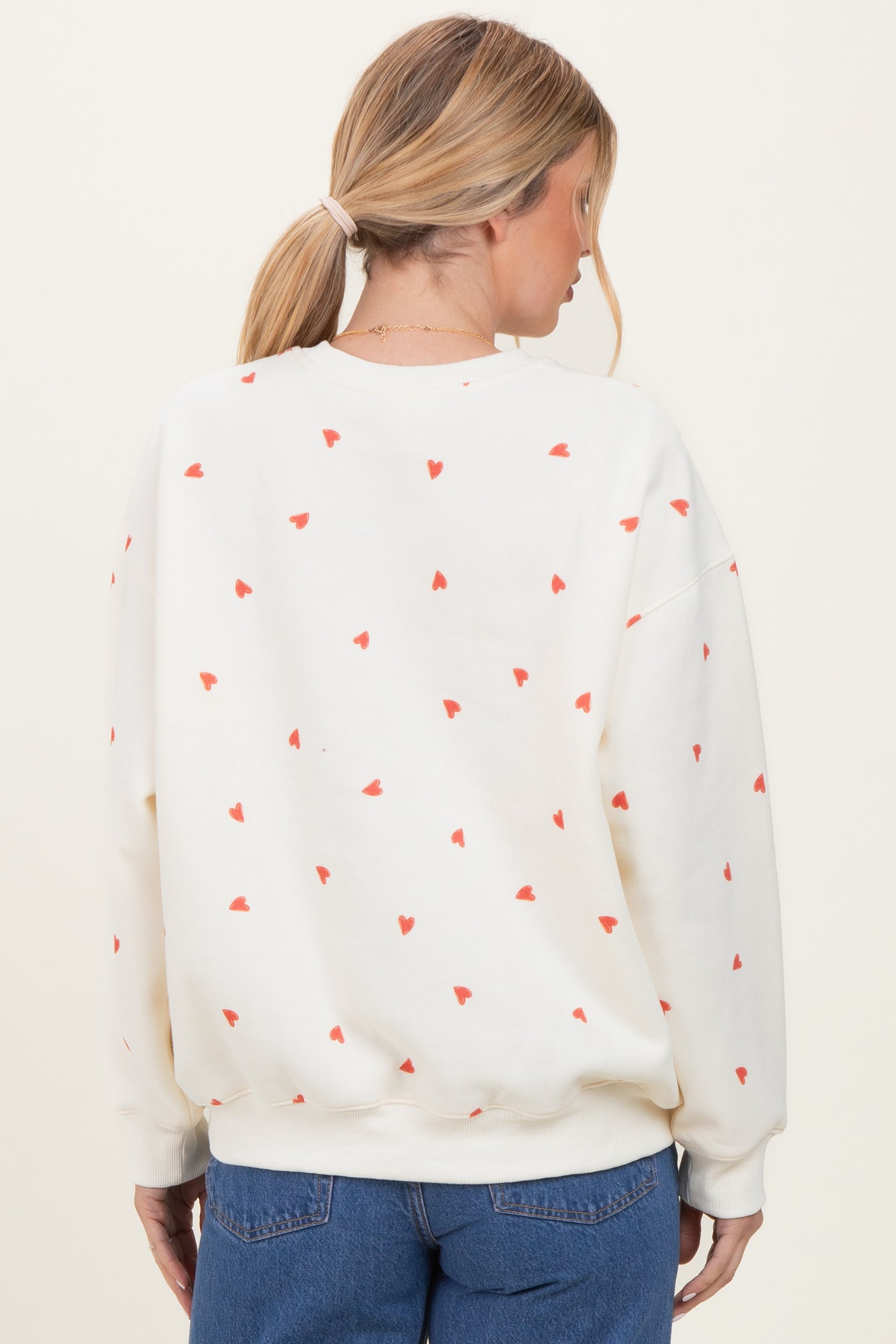 woman wearing a cream oversized sweatshirt with red heart print, viewed from the back