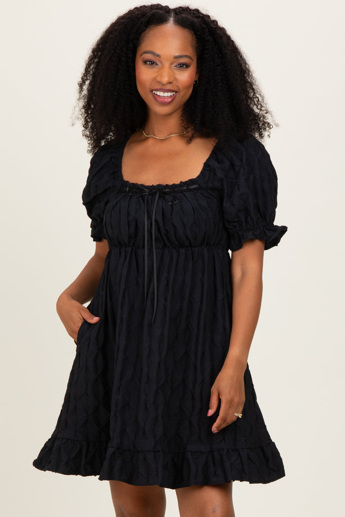 woman wearing a black short puff sleeve dress with a square neckline and ruffled hem, featuring a textured fabric