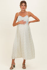 woman wearing a light floral maternity dress with adjustable straps and holding her baby bump
