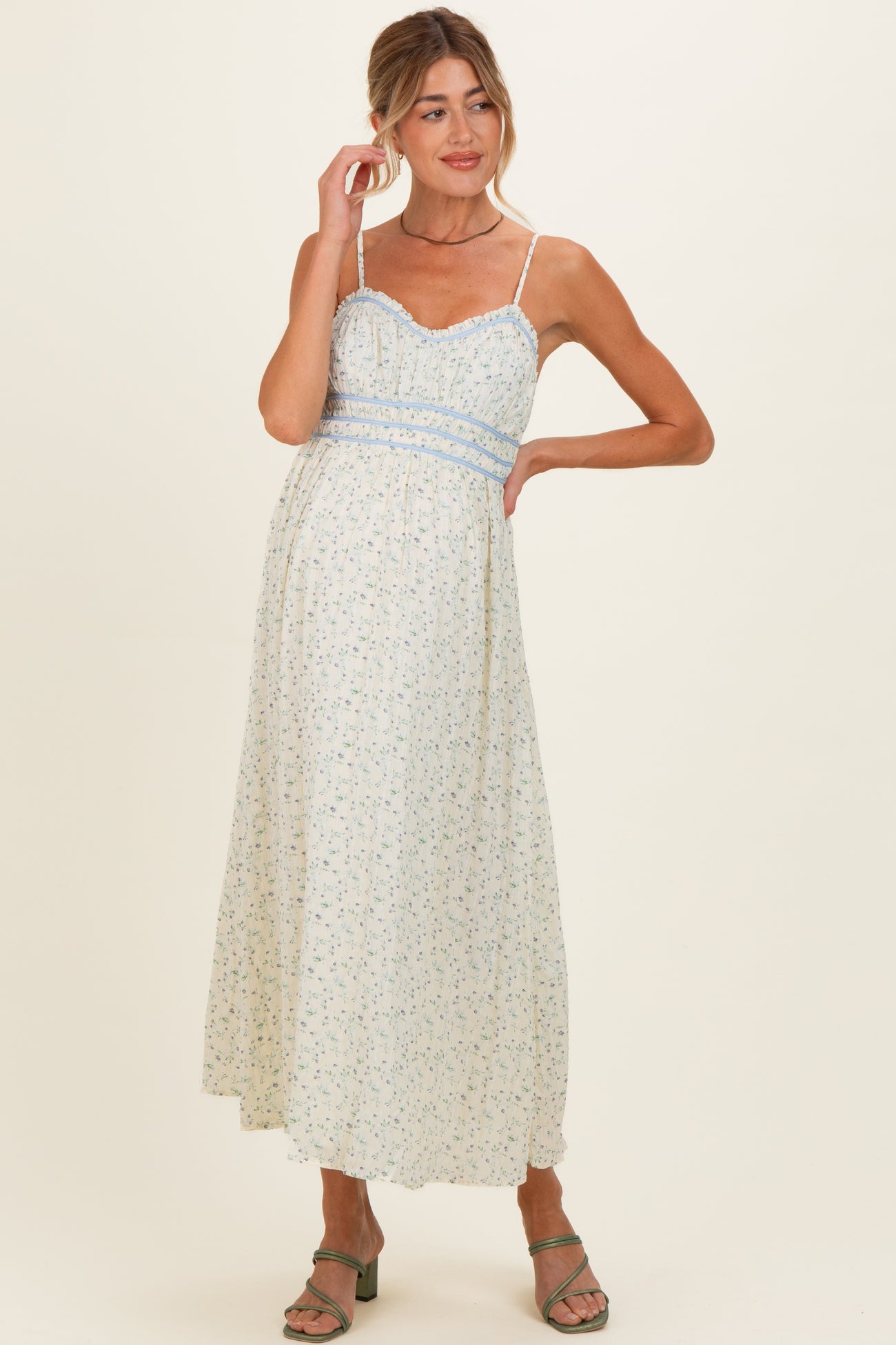 woman wearing a floral print maternity maxi dress with thin straps and a fitted bodice, gently cradling her baby bump