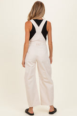 woman wearing a black tank top and light beige maternity overalls, showing a relaxed fit from the back