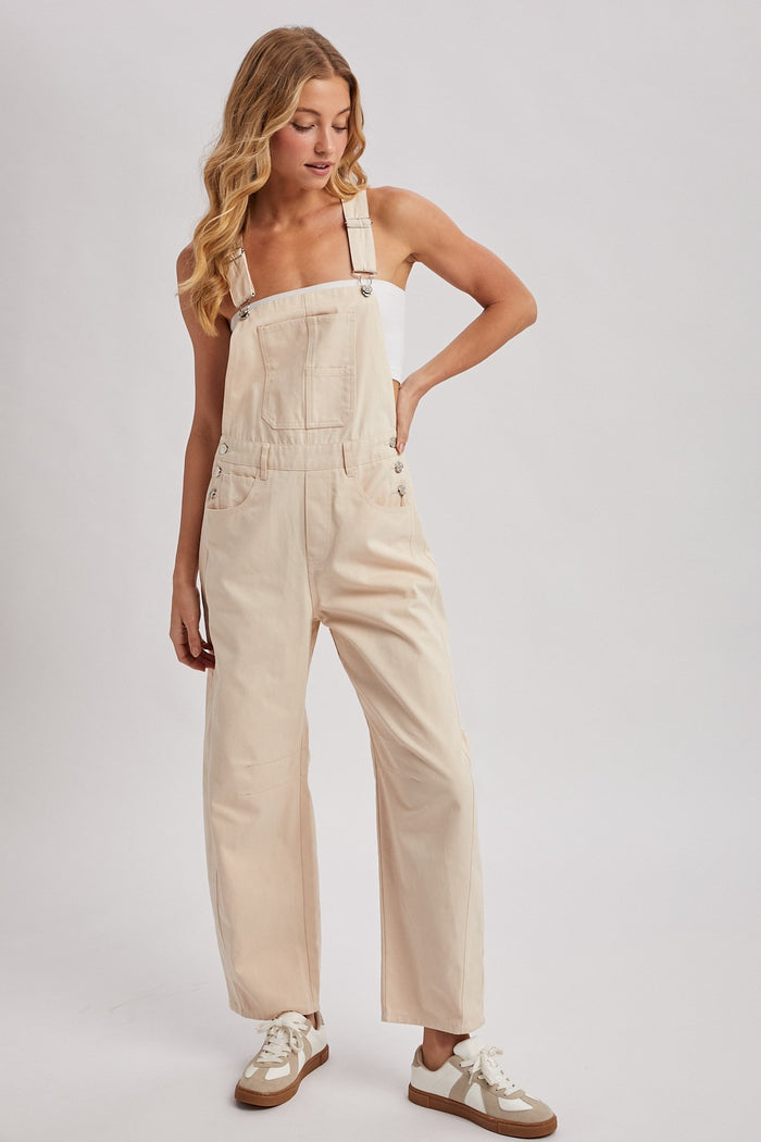 woman wearing light beige denim overalls with wide legs and adjustable straps, styled with a white top and sneakers