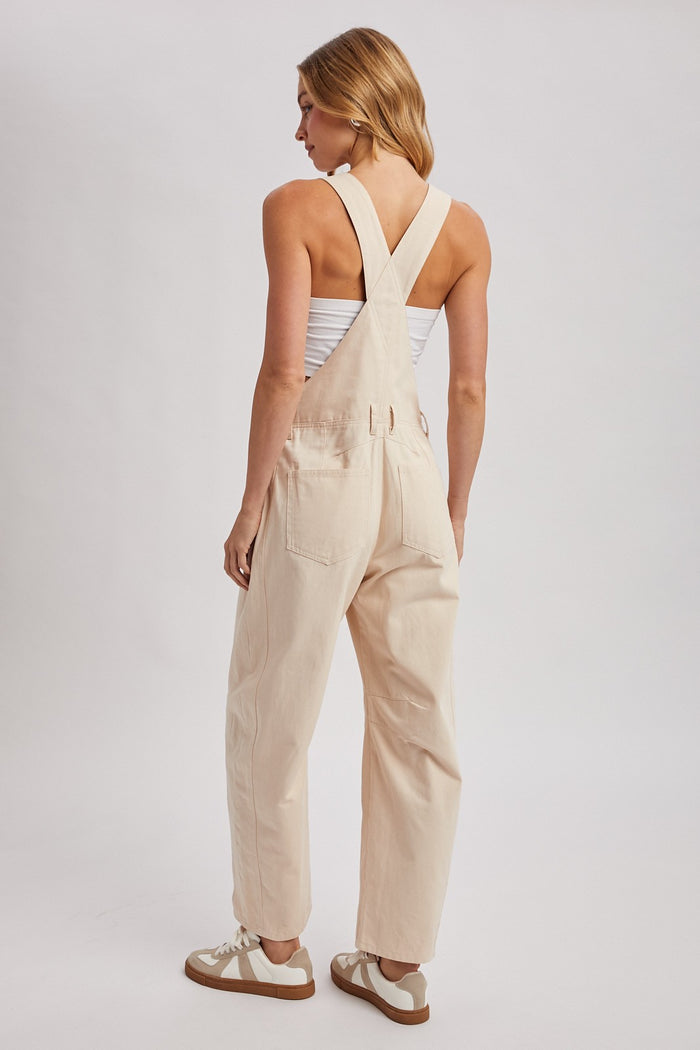 woman wearing a light beige overall jumpsuit with a fitted bodice and relaxed fit legs, viewed from the back