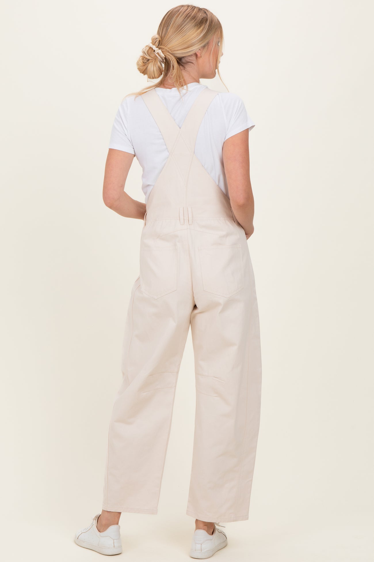 woman wearing a white t-shirt and beige overalls, showing the back view with a loose fit and adjustable straps