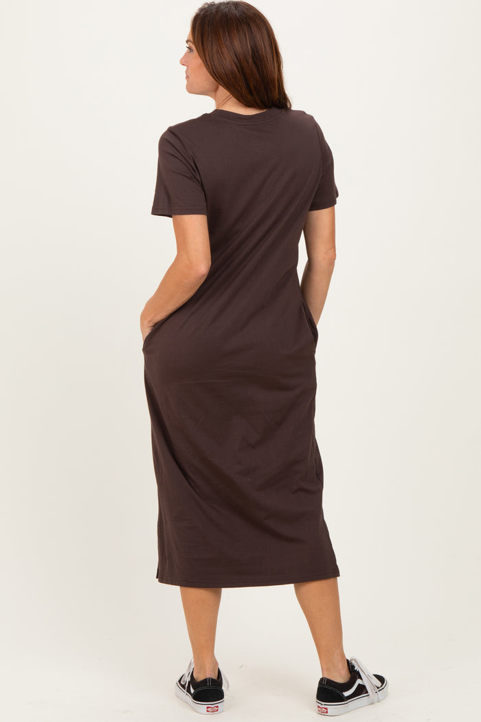 woman wearing a brown short sleeve maxi dress with pockets, standing with her back to the camera