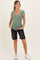 woman wearing a light green ribbed short sleeve maternity top and black denim shorts, showing her baby bump